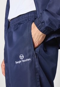 Navy Trainingsanzug aus strukturiertem Stoff, mit elastischem Bund und Bündchen. Mit gesticktem "Sergio Tacchini"-Logo und mit Reißverschlüssen versehenen Taschen.