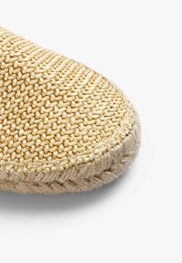 Naturligt vævet espadrille i en lys tan-farve, med struktureret overflade, rund tå og jute-detaljer langs sålen.