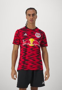 Maglia da calcio a zigzag rossa e nera con collo tondo, caratterizzata dal logo Red Bull e dalle strisce bianche Adidas sulle spalle.