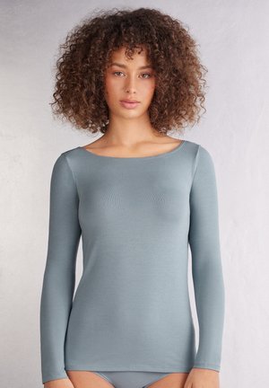Lange mouwen, getailleerde top in gedempt blauw, gemaakt van zachte, rekbare stof. Heeft een brede halslijn en naadloze constructie voor extra comfort.