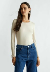 Top crema a maniche lunghe con scollo ondulato e silhouette aderente, abbinato a jeans in denim blu a vita alta.