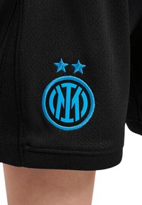 Crne kratke hlače imaju vezeni plavi logo s dvije zvijezde iznad, prikazujući detaljno šivanje i teksturiranu tkaninu.