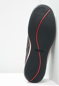 Schwarze Gummisohle mit einem wellenförmigen Profil, ausgestattet mit einem auffälligen rot-weißen Streifen an der Seite und geprägtem "SEBAGO"-Logo.