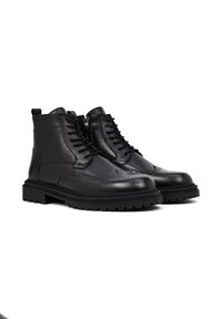 Zwarte leren enkelboots hebben brogue-details, een vetersluiting aan de voorkant, ritssluiting, een getextureerde zool en een robuuste constructie.