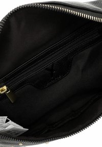 Wnętrze czarnej skórzanej torby z kieszenią na zamek błyskawiczny, gładką fakturą i elementami w kolorze złota. Ściany wyłożone są ciemną tkaniną.