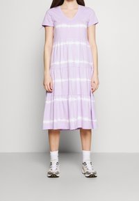 Lavendelfärgad bomullsklänning med V-ringning, korta ärmar, lagerdesign och vita batikstrimmor. Bärs med grå och vita sneakers.