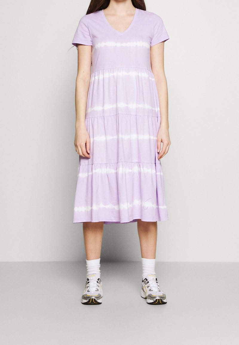 Lavendelfärgad bomullsklänning med V-ringning, korta ärmar, lagerdesign och vita batikstrimmor. Bärs med grå och vita sneakers.