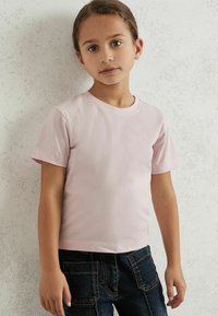 Lyserød bomulds T-shirt med korte ærmer og rund halsudskæring, parret med mørkeblå jeans med orange syninger og lommer.