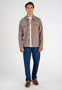 Grå knäppskjorta med två bröstfickor, bärs över en vit t-shirt, kombineras med blå denimjeans och bruna snörskor.