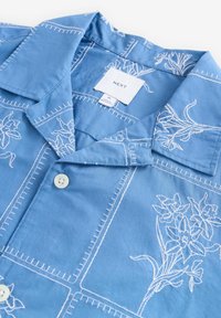 Lichtblauw shirt met witte bloemenborduursels, knoopsluiting en gestructureerde kraag. Gladde stof met contrasterende stikdetails.