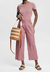 Lichtroze getailleerd T-shirt, hooggewaisted lichtroze linnen wijde broek, geweven strooien en bruin gestreepte schoudertas, tan sandalen.