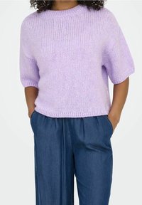 Maglione lilla lavorato a maglia con scollo rotondo e maniche corte, abbinato a pantaloni in denim blu larghi. Tessuto morbido e vestibilità rilassata.