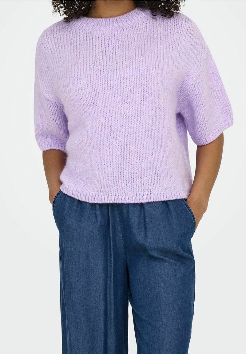 Maglione lilla lavorato a maglia con scollo rotondo e maniche corte, abbinato a pantaloni in denim blu larghi. Tessuto morbido e vestibilità rilassata.
