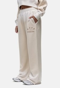 Beige joggingbroek met een elastische tailleband en zijzakken. Heeft scripttekst "goed voor niets" in een subtiele, contrasterende kleur.