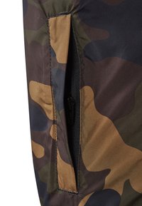 Camo-patterned fabric with green, brown, and black tones; features a zippered pocket with a concealed pull tab and a textured finish.