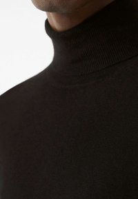 Svart polokrage tröja i ett mjukt, stretchigt stickat tyg. Har hög krage och smal passform, vilket framhäver en minimalistisk design.