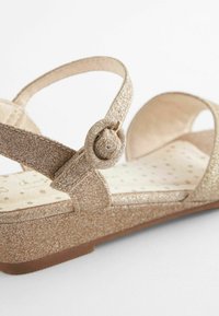 Glittery gouden wedge sandaal met kruiss straps, ronde gespsluiting, gewatteerde binnenzool met sterpatroon en een gestructureerd oppervlak.