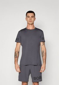 Camiseta deportiva gris con el logotipo negro "BORG" en la manga izquierda, combinada con pantalones cortos a juego que tienen una impresión lateral. Material suave y que absorbe la humedad.