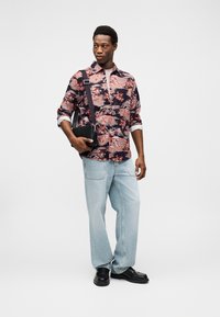 Πουκάμισο με μοτίβο λουλουδιών σε σκούρα χρώματα, τζιν με ανοιχτό πλύσιμο, μαύρη τσάντα χιαστί και μαύρα παπούτσια με χοντρή σόλα.