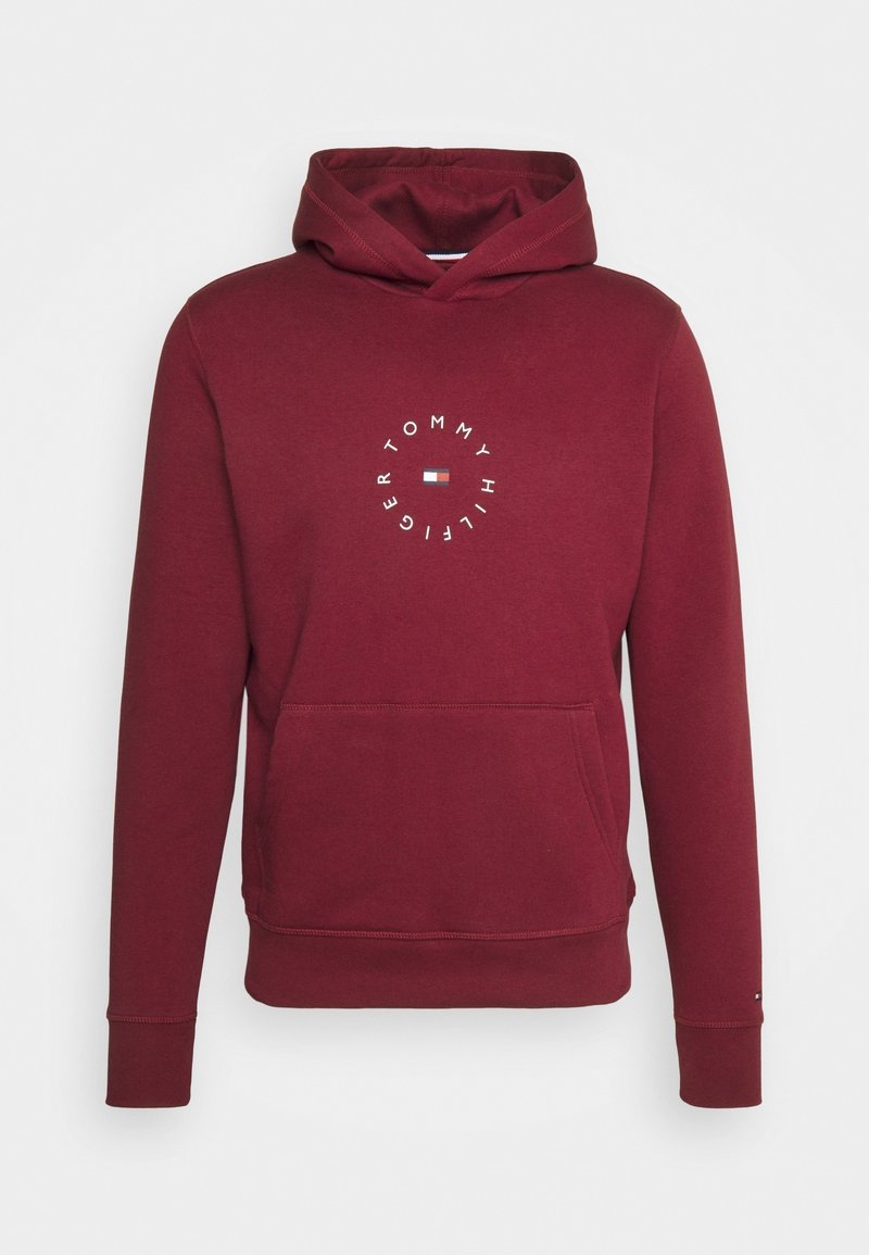 Sweat à capuche bordeaux avec poche kangourou devant et logo circulaire "Tommy Hilfiger" entourant le drapeau de la marque au centre de la poitrine.