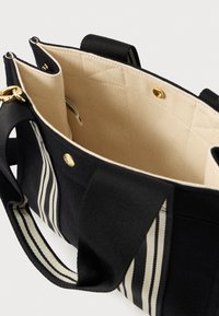Borsa tote in tela nera con interno color crema, dettagli in tessuto a righe, finiture in oro e manici robusti per un facile trasporto.