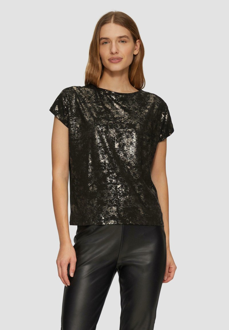 Schwarzes Kurzarmoberteil mit glänzender, strukturierter Oberfläche, mit lockerem Schnitt und gerundetem Ausschnitt, kombiniert mit schwarzen, lederähnlichen Hosen.