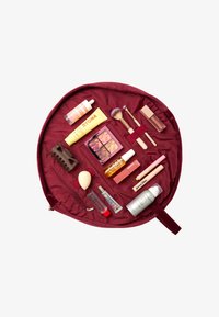 Bolsa de maquillaje redonda de color burdeos abierta, con varios cosméticos que incluyen botellas, una paleta, brochas y una esponja organizados de manera ordenada en su interior.