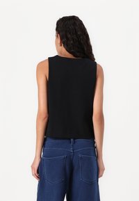 Black sleeveless top with a round neckline, made of smooth fabric; features a cropped cut and is paired with blue denim wide-leg pants.