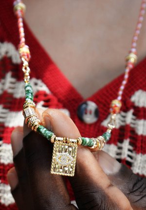 Goldfarbener Halsreifen mit einem rechteckigen Anhänger, der ein Diamant-Augen-Design zeigt, geschmückt mit grünen Perlen und mehrfarbigen Akzenten.