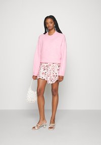 Sweater rosa de malha com mangas longas, combinado com calções florais em creme claro. Sandálias de salto brancas e uma bolsa texturizada.
