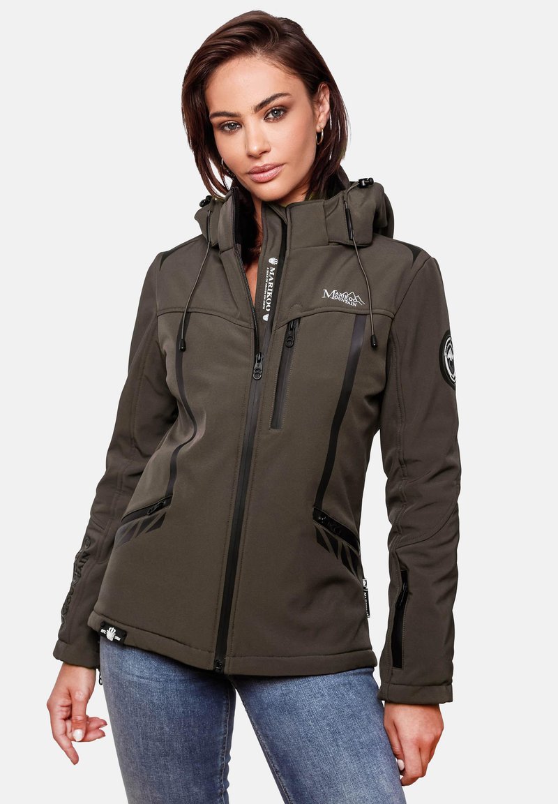 Woman wearing a dark green hooded softshell jacket with zippered pockets, standing against a plain light background.