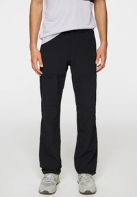 Czarne, lekkie spodnie o prostym kroju, z bocznymi kieszeniami i gładką fakturą, w połączeniu z jasnoszarymi sneakersami.