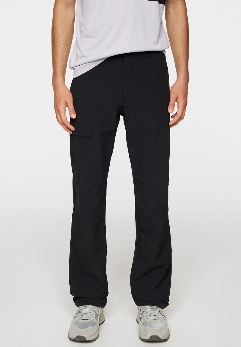 Czarne, lekkie spodnie o prostym kroju, z bocznymi kieszeniami i gładką fakturą, w połączeniu z jasnoszarymi sneakersami.