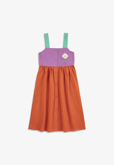 Robe sans manches avec bretelles vertes, corsage violet ornée d'une fleur blanche pixellisée, et jupe orange à boutons.