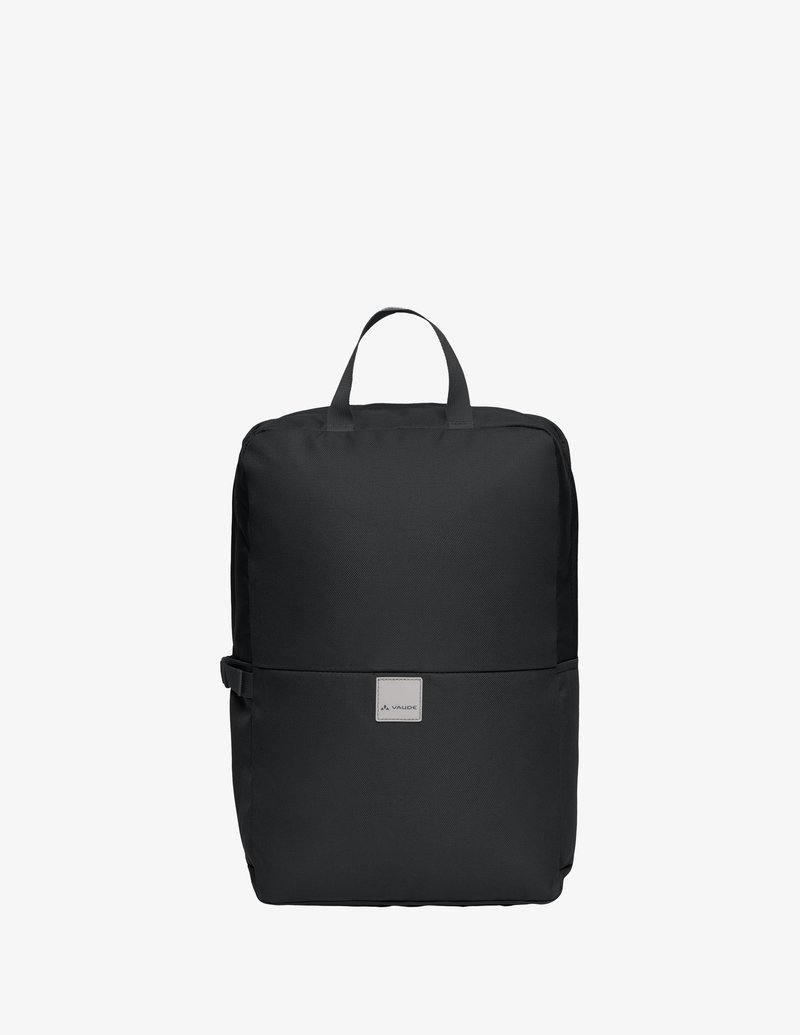 Mochila rectangular de tela negra con asa superior, hebilla lateral y pequeño parche de logo frontal, mostrada sobre un fondo blanco.