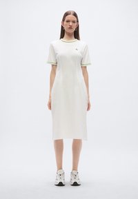 Λευκό βαμβακερό μίντι φόρεμα με κοντά μανίκια, με πράσινες λεπτομέρειες στο ντεκολτέ και τα τελειώματα των μανικιών. Το μοντέλο το συνδύασε με αθλητικά παπούτσια.