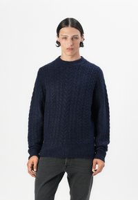 Suéter de punto trenzado en color navy, elaborado con lana gruesa, que presenta un cuello redondo y ribetes acanalados, con un patrón texturado en toda su superficie.