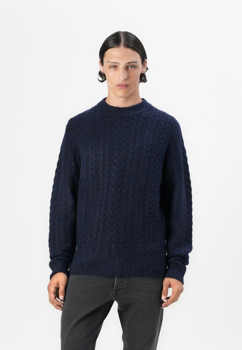 Suéter de punto trenzado en color navy, elaborado con lana gruesa, que presenta un cuello redondo y ribetes acanalados, con un patrón texturado en toda su superficie.