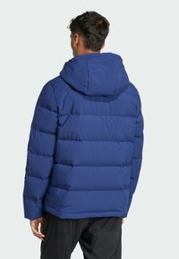 Modrá prešívaná bunda s kapucňou, s prešívanými panelmi a hladkým, lesklým povrchom. Dizajn zahŕňa rovný lem a elastické manžety.