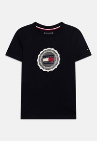 T-shirt in cotone nero con logo ricamato circolare caratterizzato da linee orizzontali e colori: rosso, bianco e blu, dettagliato con un bordo a onde.