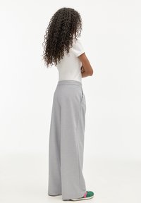 Pantalon large gris clair en tissu lisse, avec poches latérales et taille cintrée, associé à une chemise blanche et des baskets colorées.