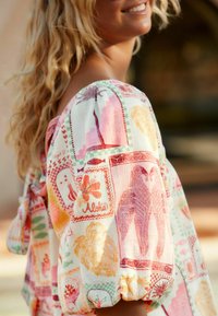 Kleurrijke, lichtgewicht stoffen top met bloemen- en dierenprints in roze, geel en groen. Heeft een pofmouw en een strikdetail aan de achterkant.