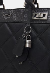 Borsa Guess in pelle trapuntata nera con charm a forma di lucchetto e chiave in argento, chiusura a girello in metallo e rifiniture superiori a motivo con logo Guess.