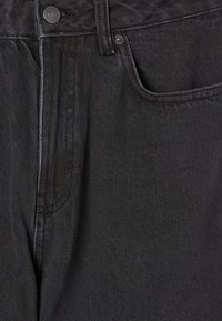 Jeans in denim nero con una vestibilità strutturata, tasca frontale, dettaglio con bottone in metallo e cuciture visibili. Texture liscia con leggero sheen.