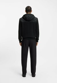 Zwarte hoodie met een gestikte schouderpaneel, geribbelde manchetten en zoom, gecombineerd met zwarte slim-fit broek. Glad stoftextuur, minimalistisch ontwerp.