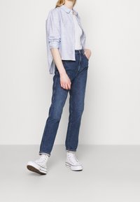Camicia button-up a quadri azzurri chiari, canotta bianca, jeans scuri a vita alta e sneakers bianche alte con dettagli neri.