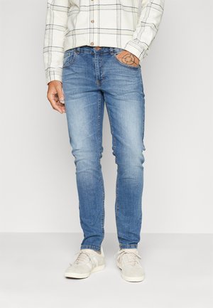 Vaqueros de mezclilla azul claro con corte ajustado, con bolsillos delanteros, sutil desgaste y costuras en contraste. Combinados con zapatillas blancas.