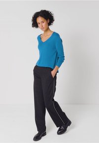 Turkos v-ringad tröja i ett mjukt material, kombinerad med mörkgrå vida byxor med vita sidostråk. Svarta läderskor.