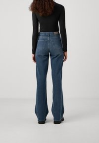 High-waisted flared jeans in medium blue denim, featuring five pockets and a subtle textured finish, with a smooth waistband and loose fit.