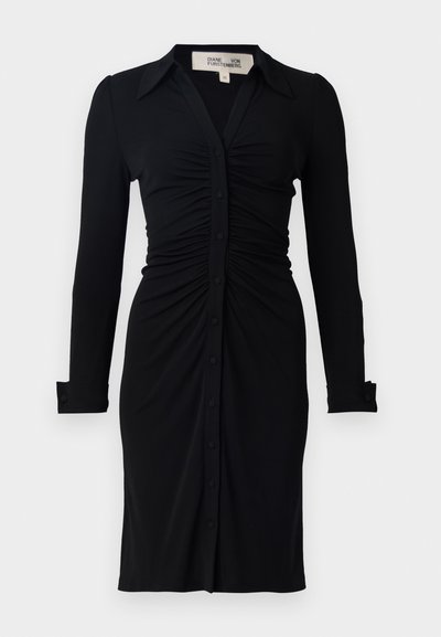 Mustassa pitkähihaisessa mekossa on kauluksessa, rypytetty vartalo ja napitus edessä, valmistettu pehmeästä kankaasta, joka on rakenteellisesti suunniteltu hihojen ja hihansuiden osalta.